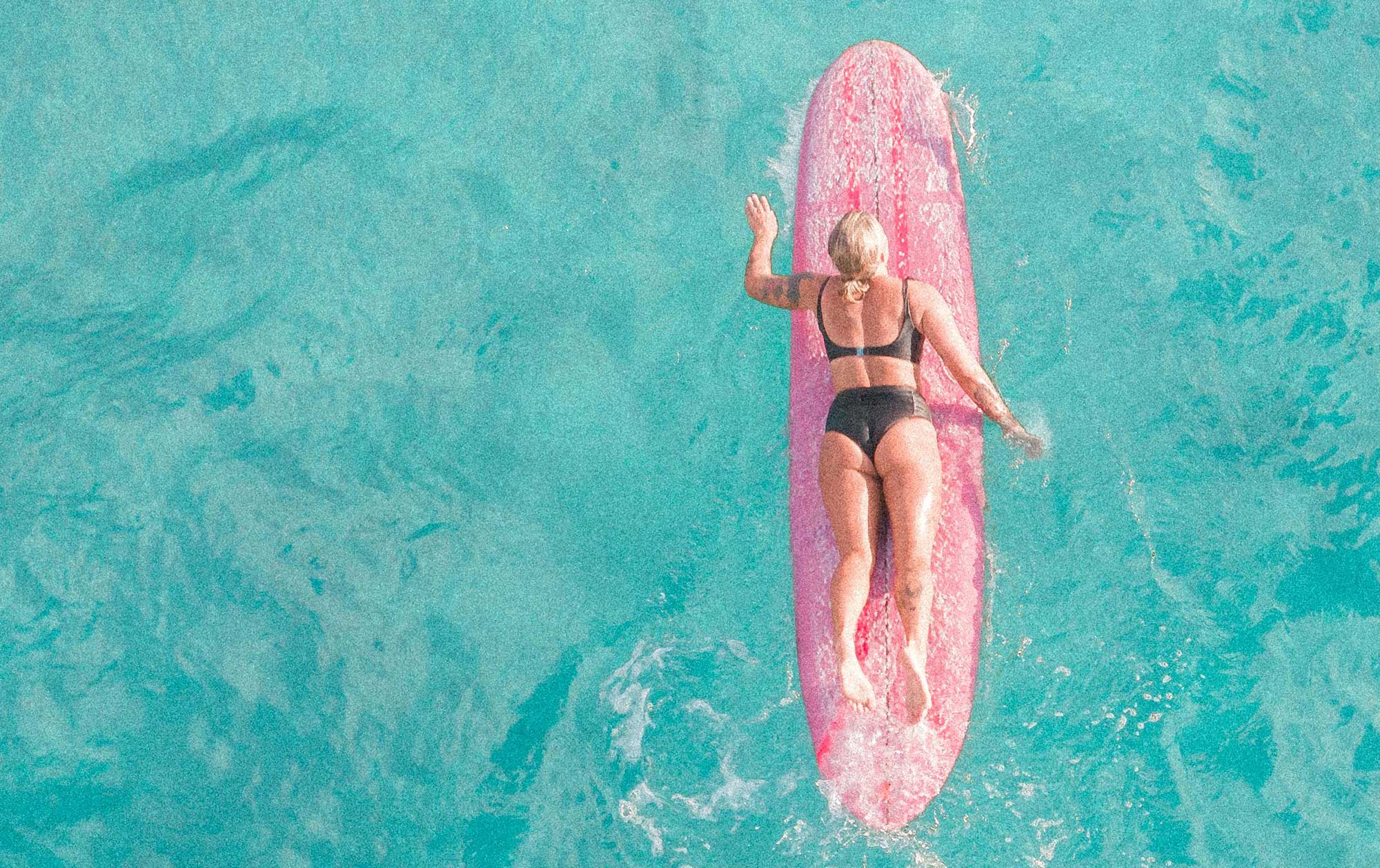 Woman on pink surfboard in ocean.